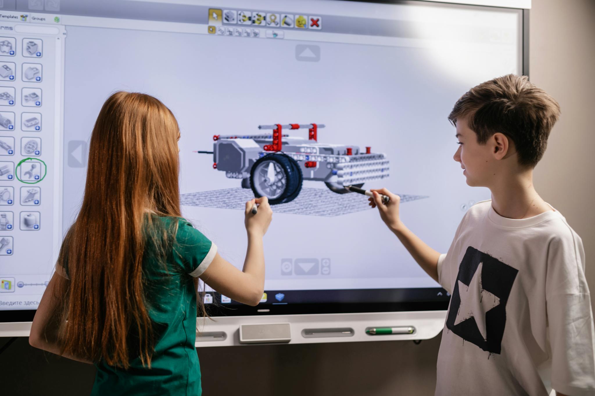 A boy and girl collaborate on a robotics project using a digital screen in a classroom setting.